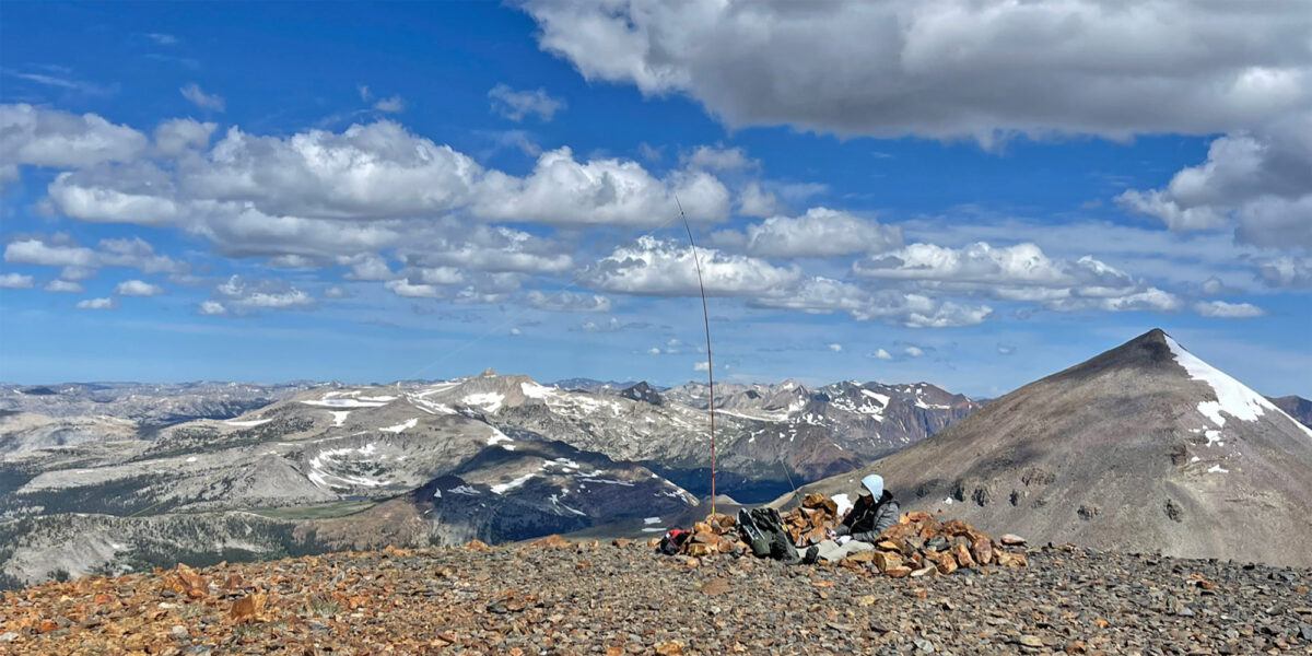 Rex, KE6MT, sitting atop Mount Gibbs operating radio, with Mount Dana and other peaks in the background
